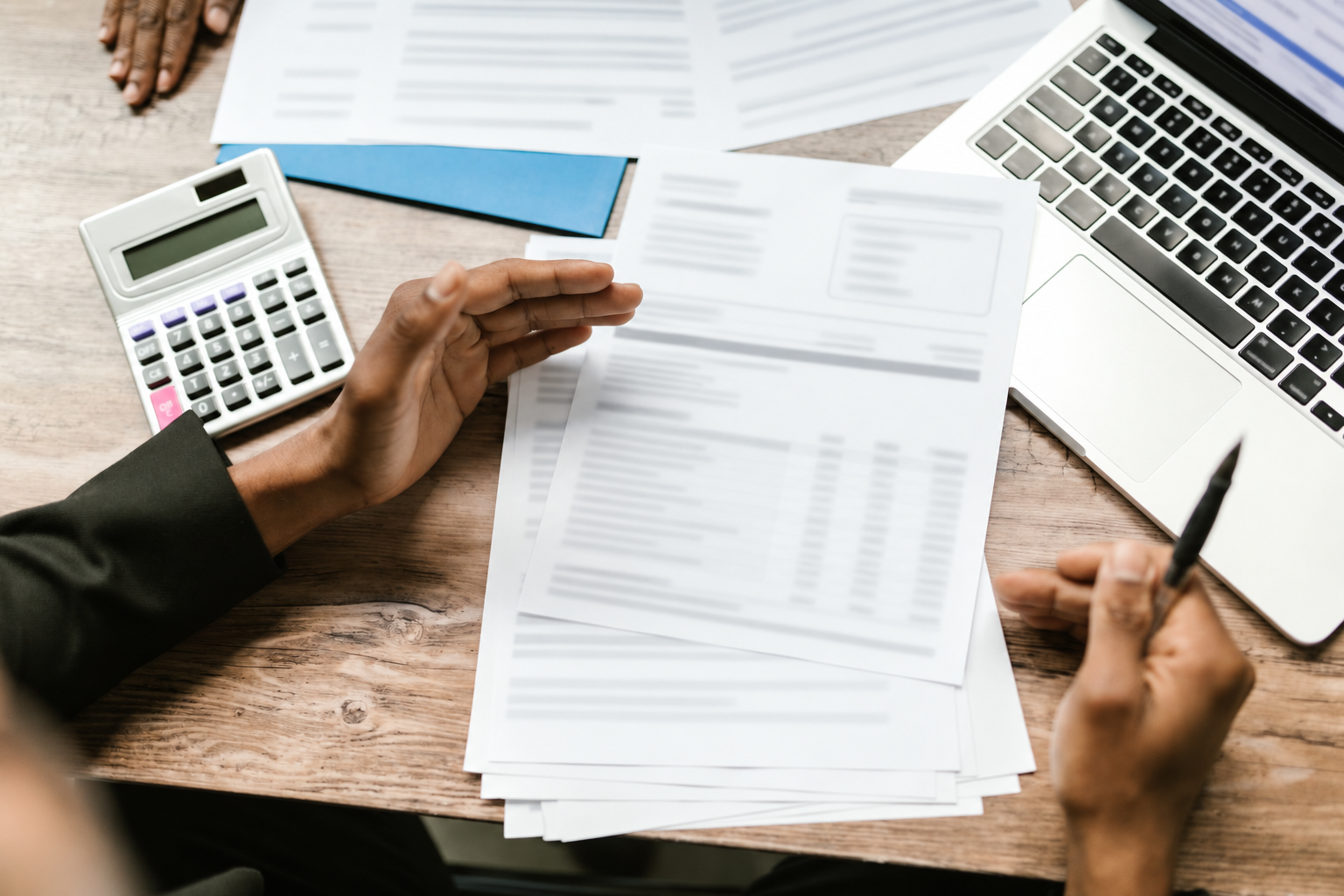Professionals reviewing financial records with a calculator and laptop